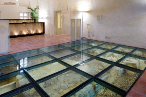 Rekonstruovaný a konzervovaný závěr kostela sv. Maří Magdaleny pod skleněnou deskou v recepci hotelových lázní (dostupné z https://pragueforadults.com/)